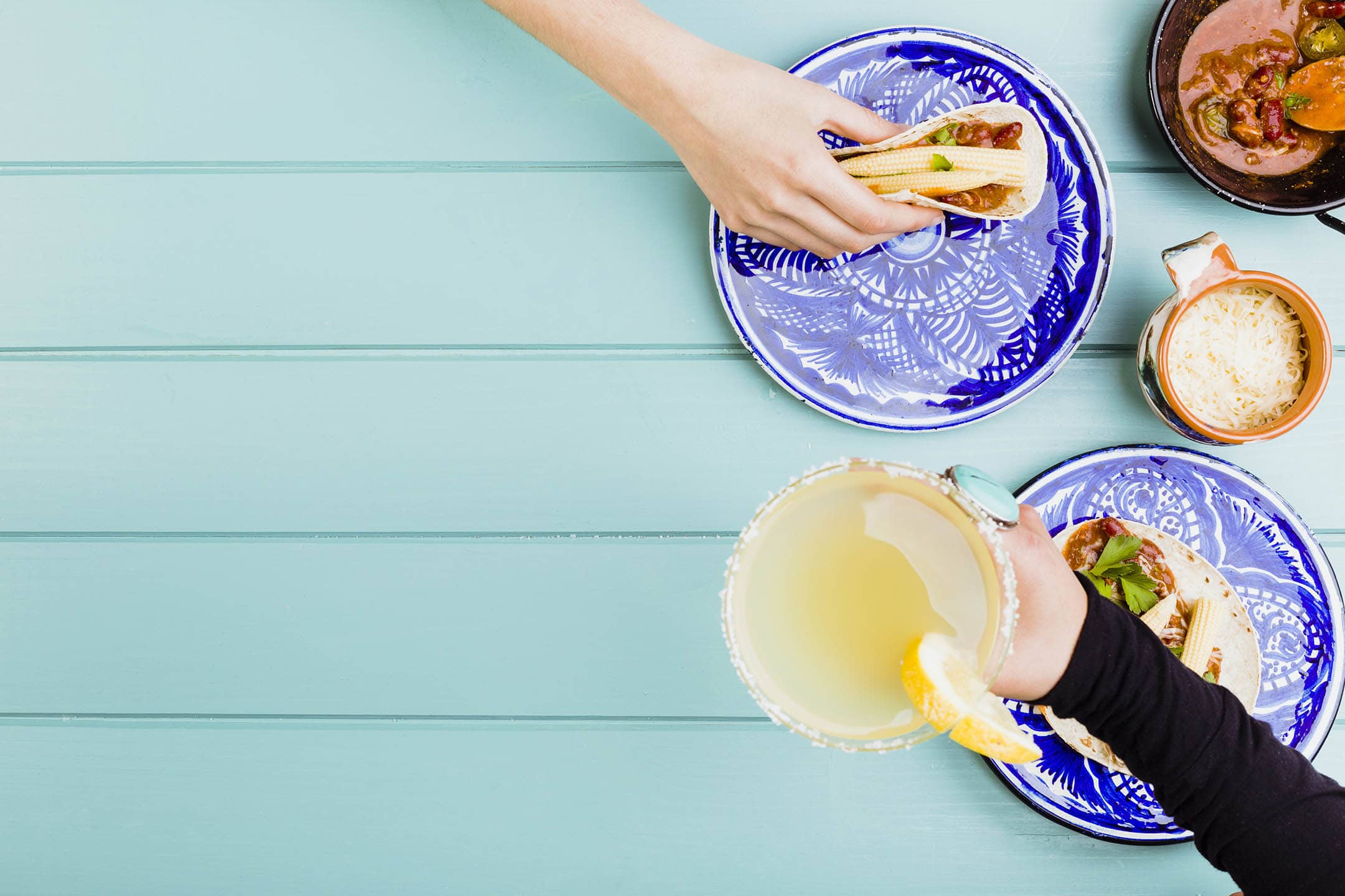 Colourful birds-eye photo of Mexican food and cocktail with people holding food and holding drink.